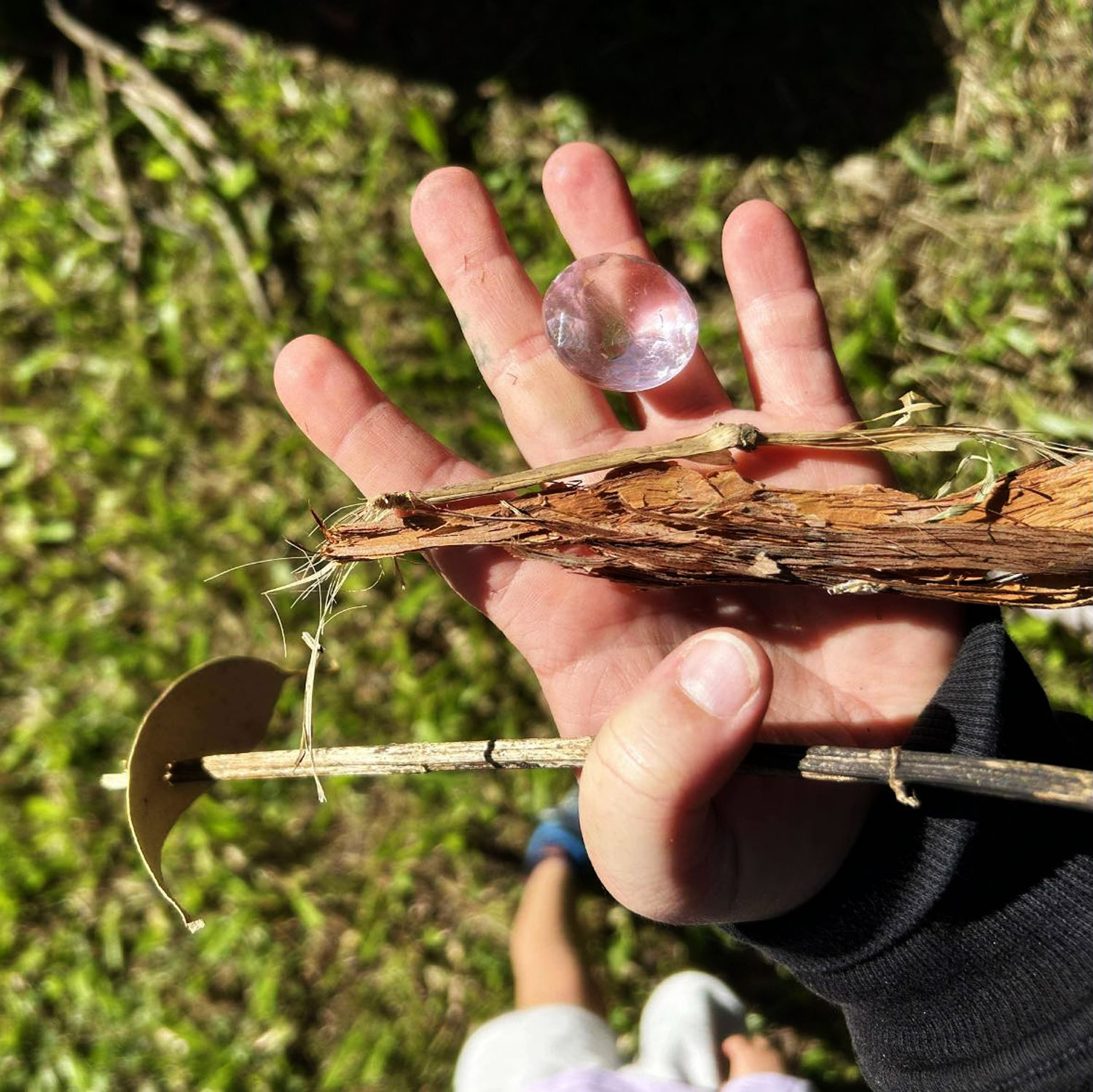 A birdseye view photography of a childs hand holding a collection of sticks and other tree material along with a plastic gem.