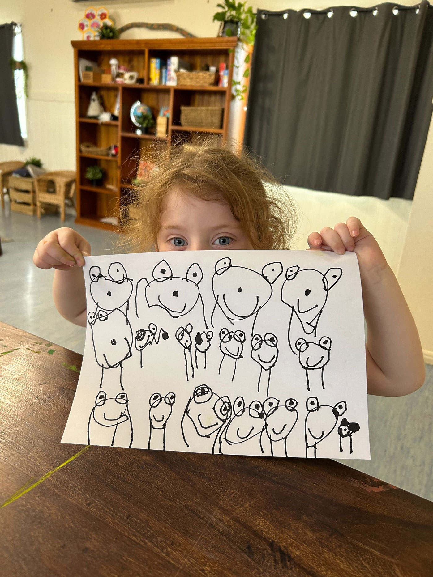 A photograph of a child holding a drawing of lots of frogs.