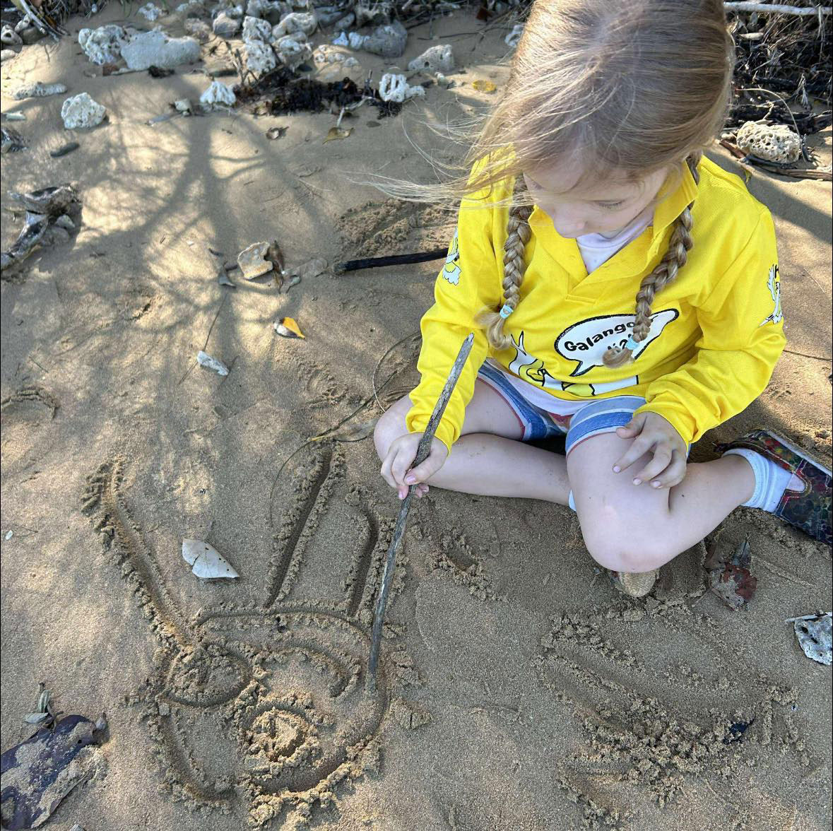 A photograph of a young child drawing a picture in the sand with a stick